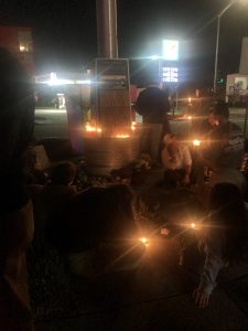 An extremely dark photo with a few candle and 7/11 lights illuminating posters and flowers left in honor of Club Q victims.