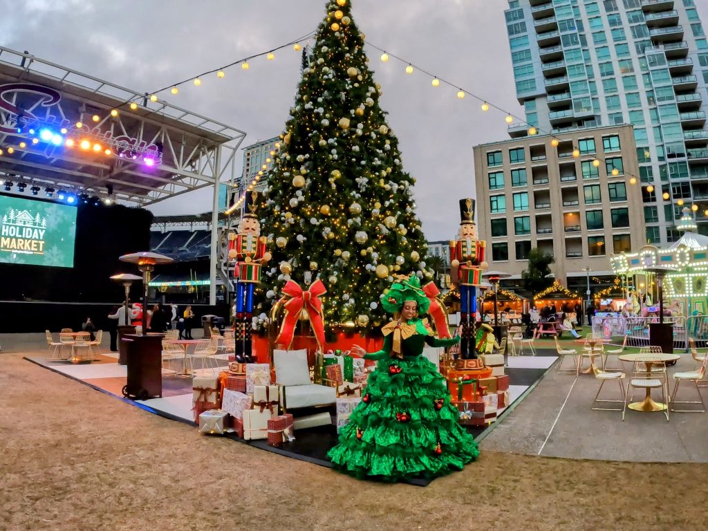 Christmas tree with lots of big presents and woman dressed in green dress at Petco Park Holiday Market San Diego