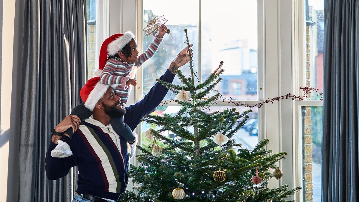 A father helping his daughter decorate their Christmas tree at home