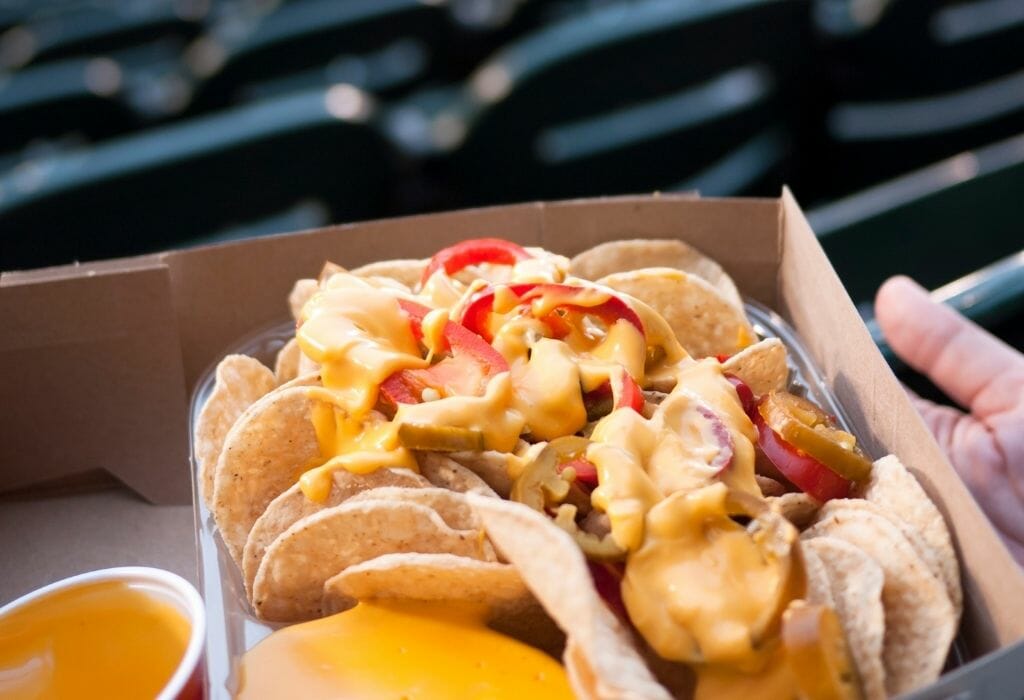 hand holding trey with nachos and cheese sauce at a baseball stadium