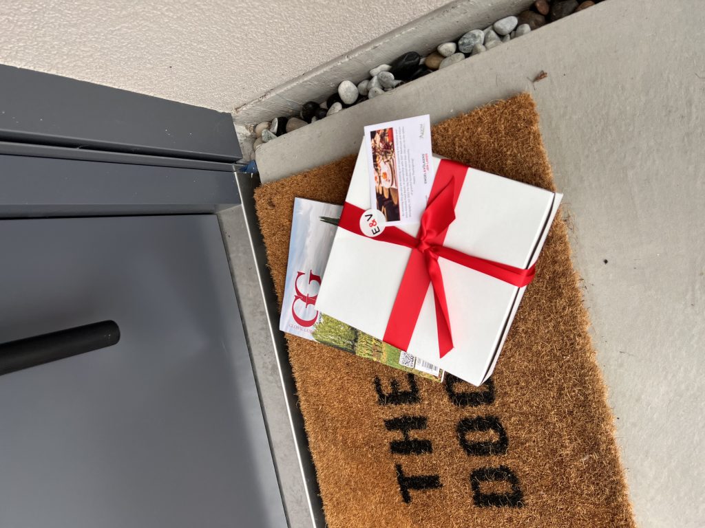 A white box wrapped in a red ribbon and an issue of GG Magazine on a doormat.