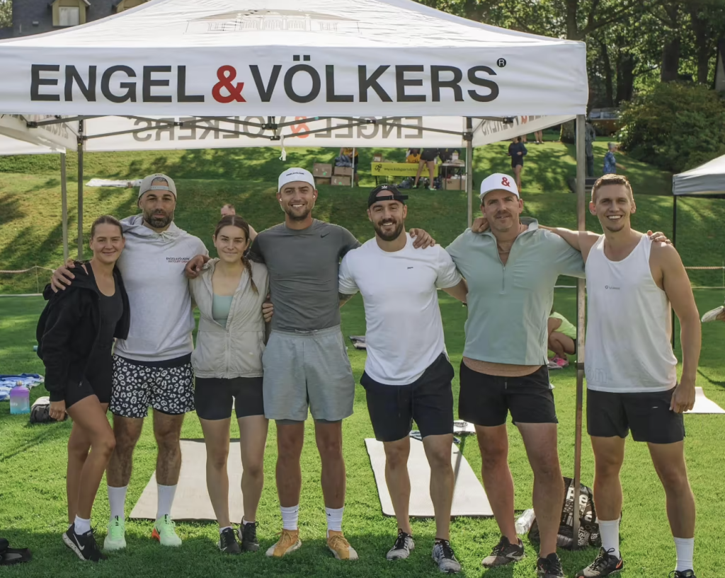 Engel & Völkers real estate advisors under a white, branded tent after a charity event in athletic attire.