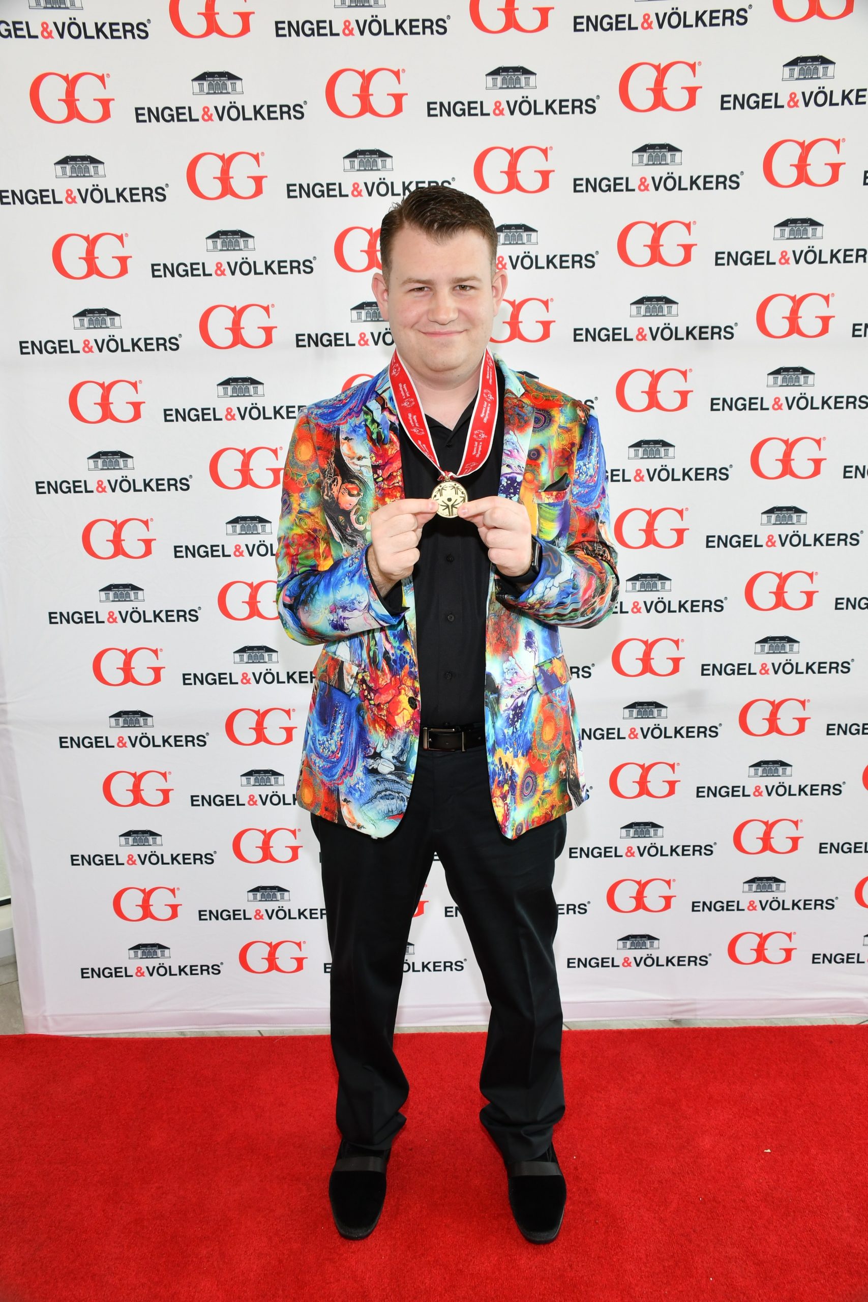 Man with a medal around his neck on the red carpet of an Engel & Völkers Tampa Downtown charity event in front of a branded step-and-repeat.