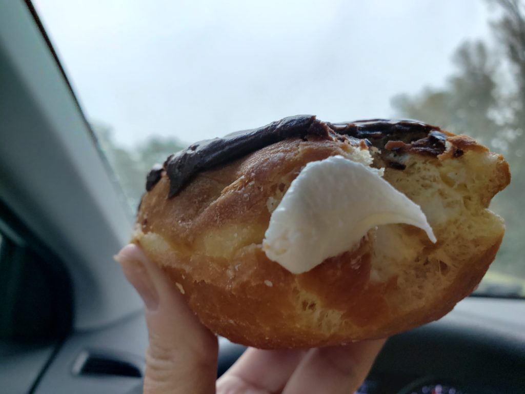 creme filled chocolate iced doughnut being eaten in the car