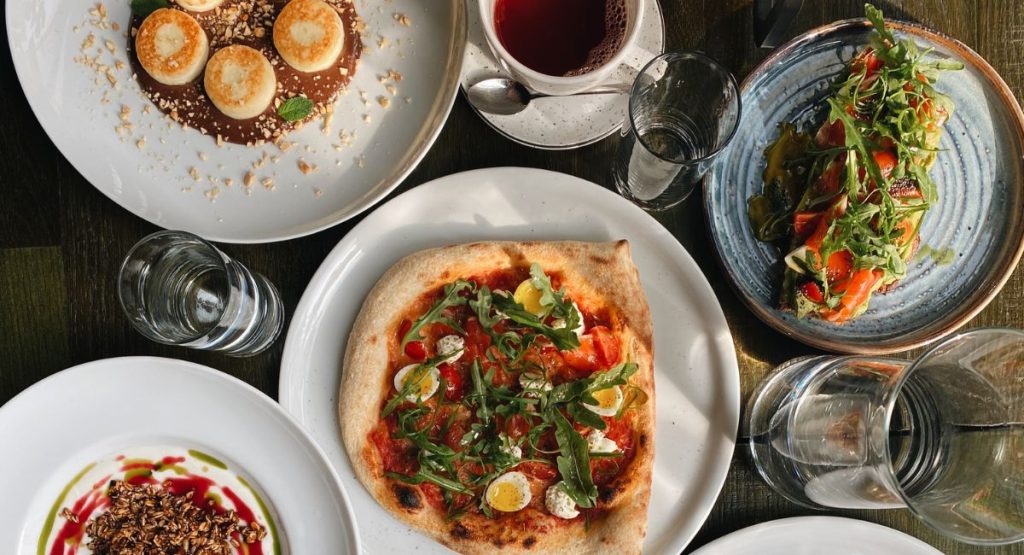 Photo of pizza and Italian food on wooden table surrounded by glassware at restaurant. Food tours San Diego.