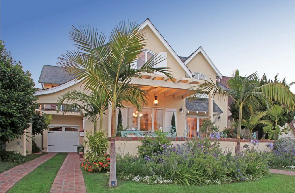 Peach-colored Coronado vacation rental with brick driveway and a palm tree in the front