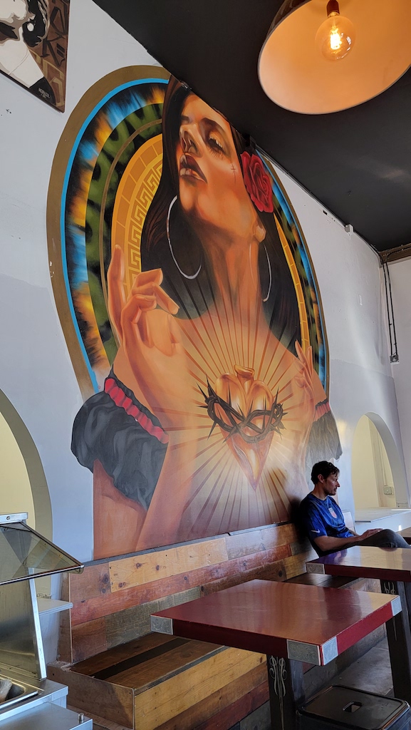 Colorful mural inside restaurant of woman in front of colorful background. Salud! Tacos, Barrio Logan Restaurants.