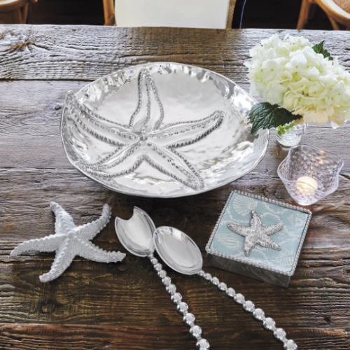 silver serving dish with a starfish on it, surrounded by serving utencils