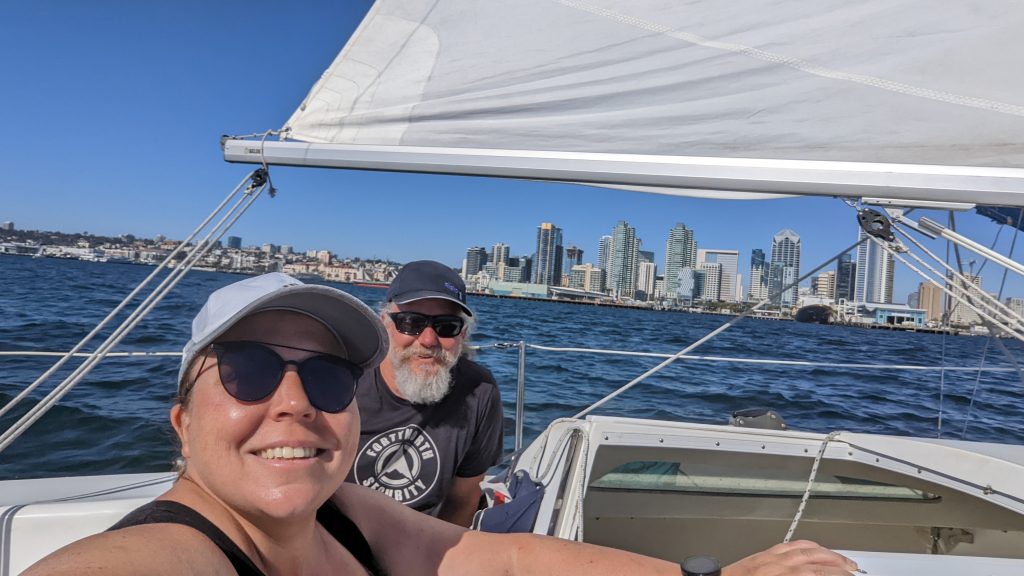 A couple on a sailboat sailing on the san Diego bay in front of the San Diego skyline