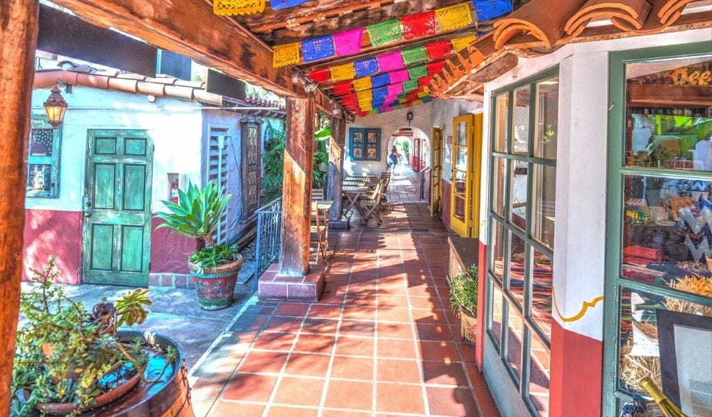 store fronts with terracotta tile walkway, white walls, wood covered path and colorful paper garlands