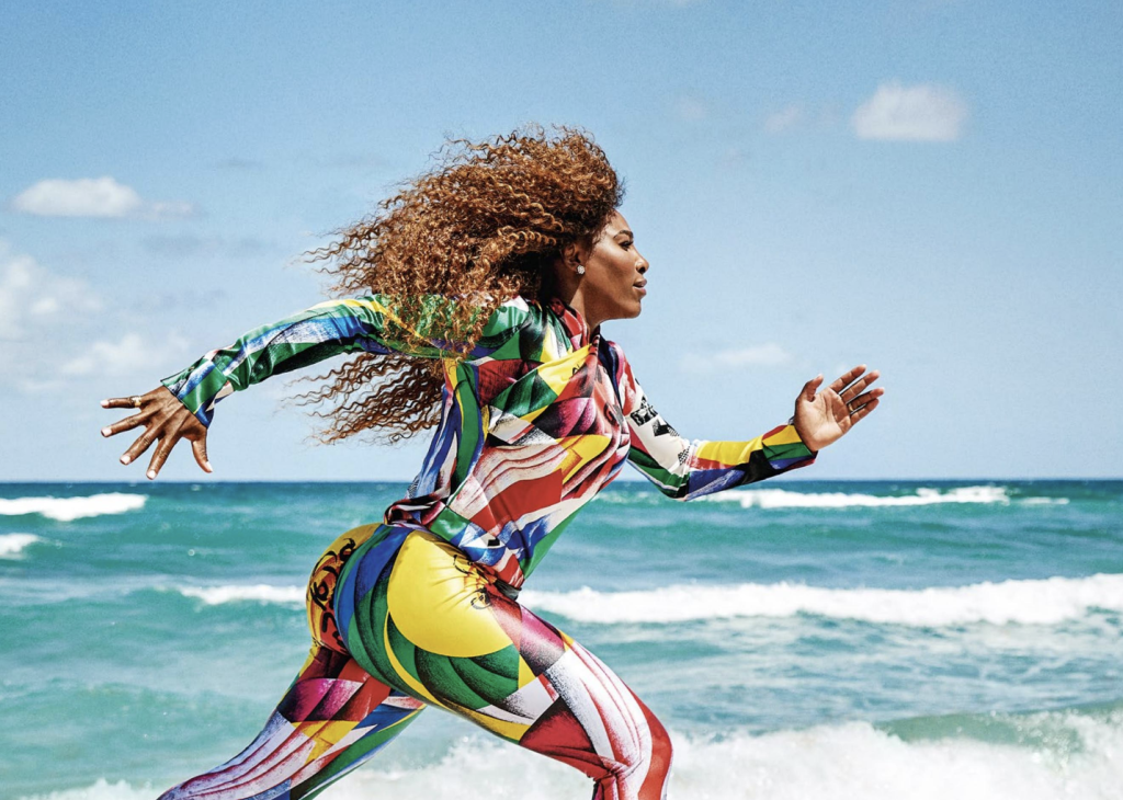 Serena Williams running on the beach in a graphic, multicolored catsuit.