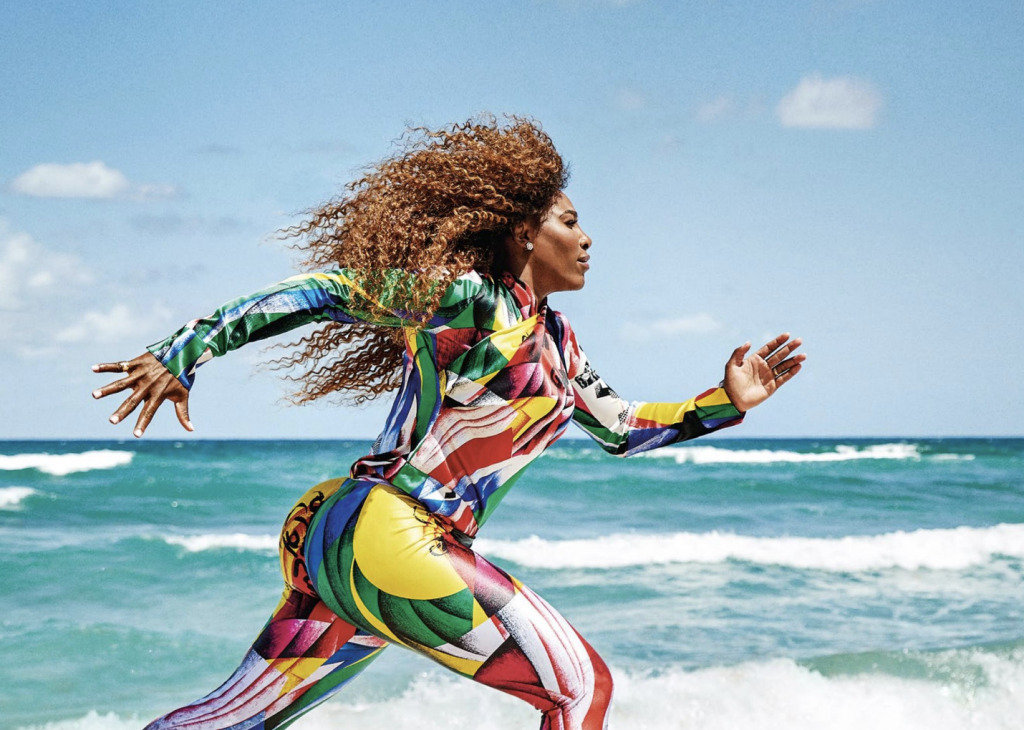 Serena Williams running on the beach in a graphic, multicolored catsuit. 