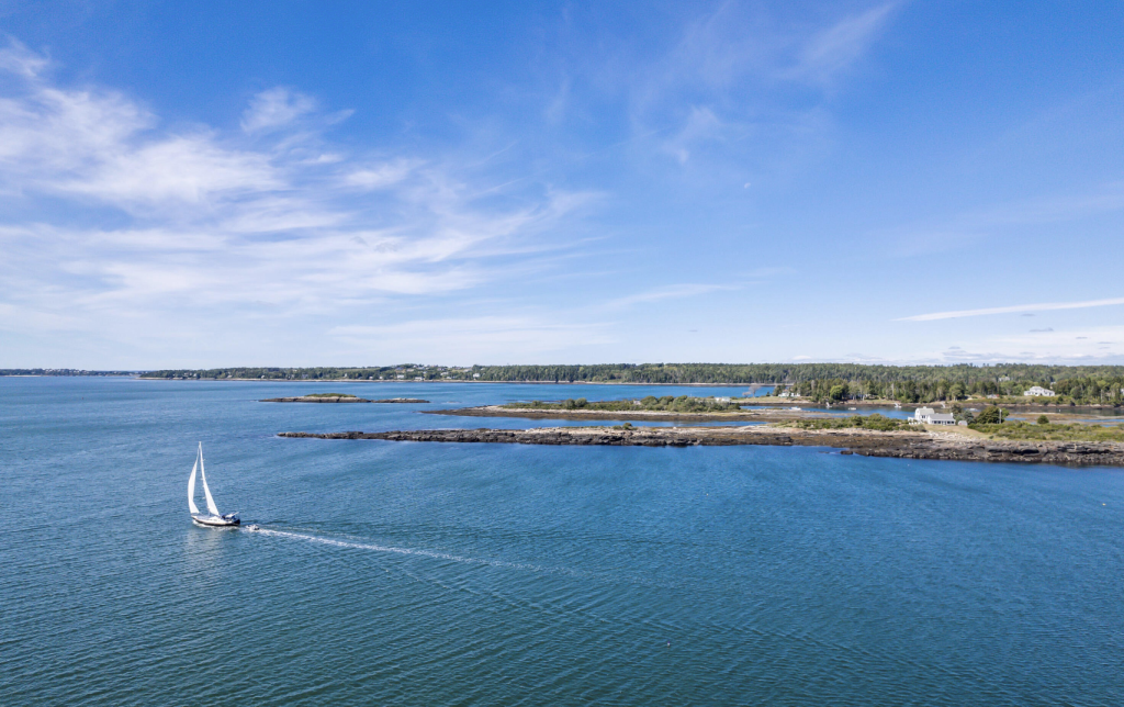 A zoomed out view of a private island with a boat sailing in the foreground.