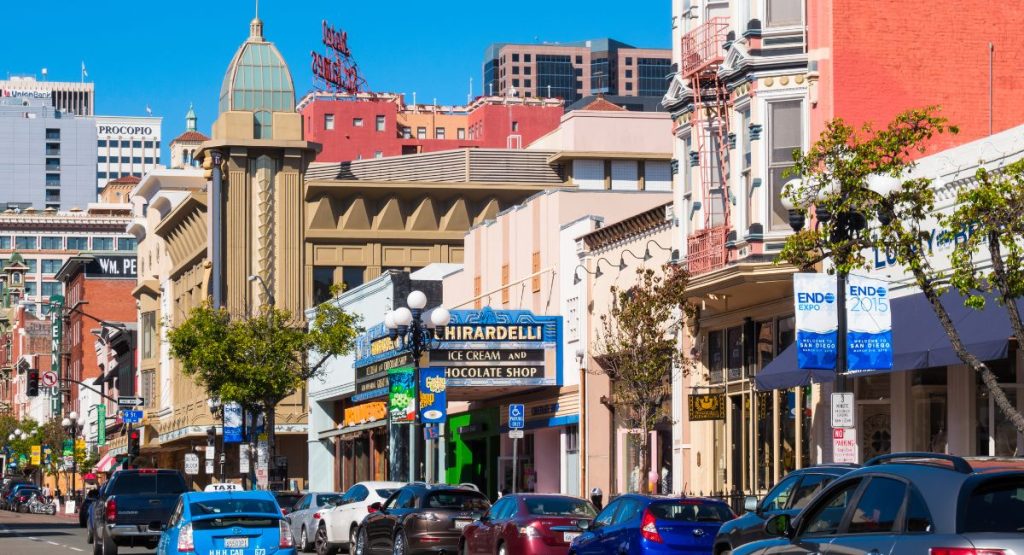 Colorful buildings lining busy street lined with cars on sunny day. 5th Avenue, Downtown San Diego, Gaslamp Quarter. Walking Tours San Diego.