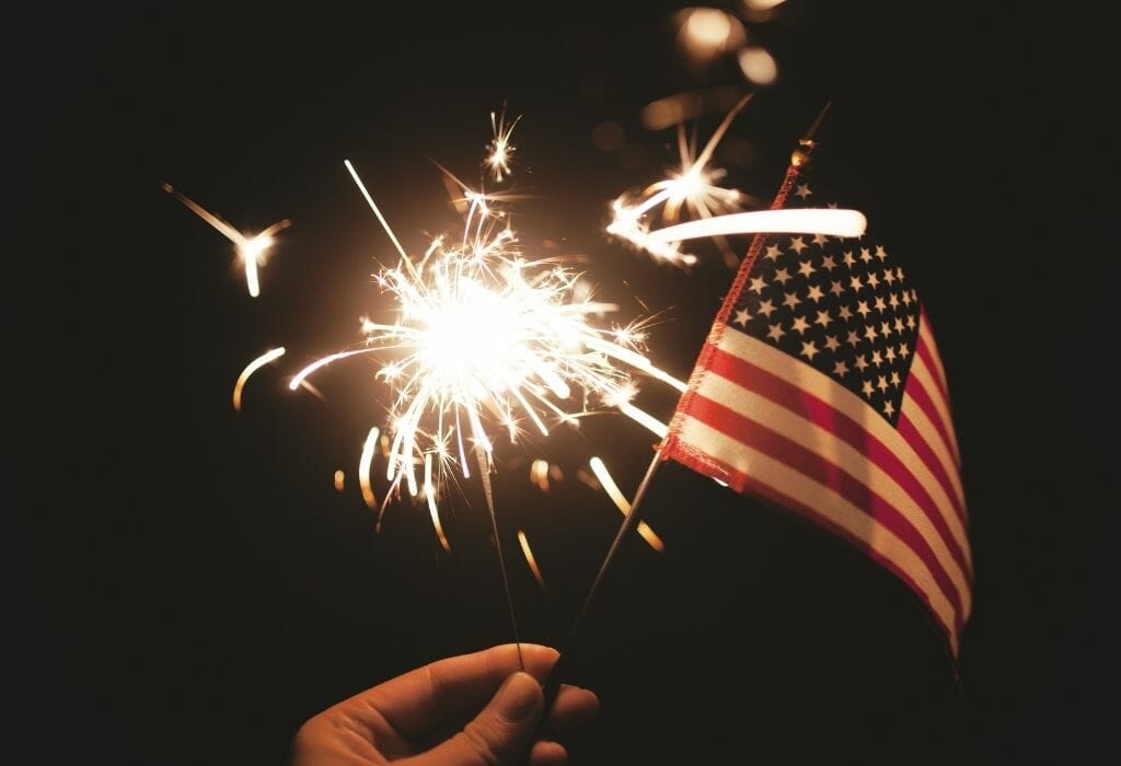 hand holding a mini American flag and a sparkler in the dark