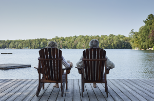 Couple sitting in Adirondack chairs in front of a lake and forest.