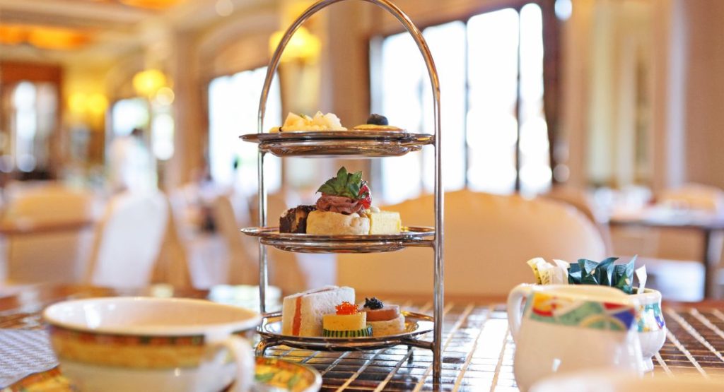 Metal tiered tray with finger snacks and pastries on table with tea set in large tea room. Afternoon tea in San Diego.