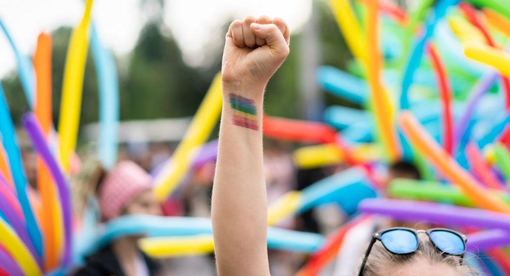 Woman standing in pride festival parade with rainbow flag on wrist