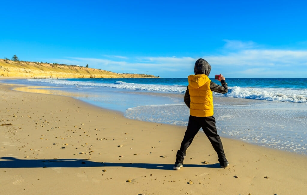 Kid in yellow jacket taking pictures of the beach