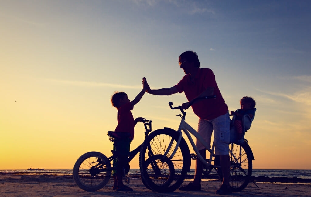 Silhouette of Adult with 2 kids and bikes on the beach at sunset - San Diego Free Kids Activities