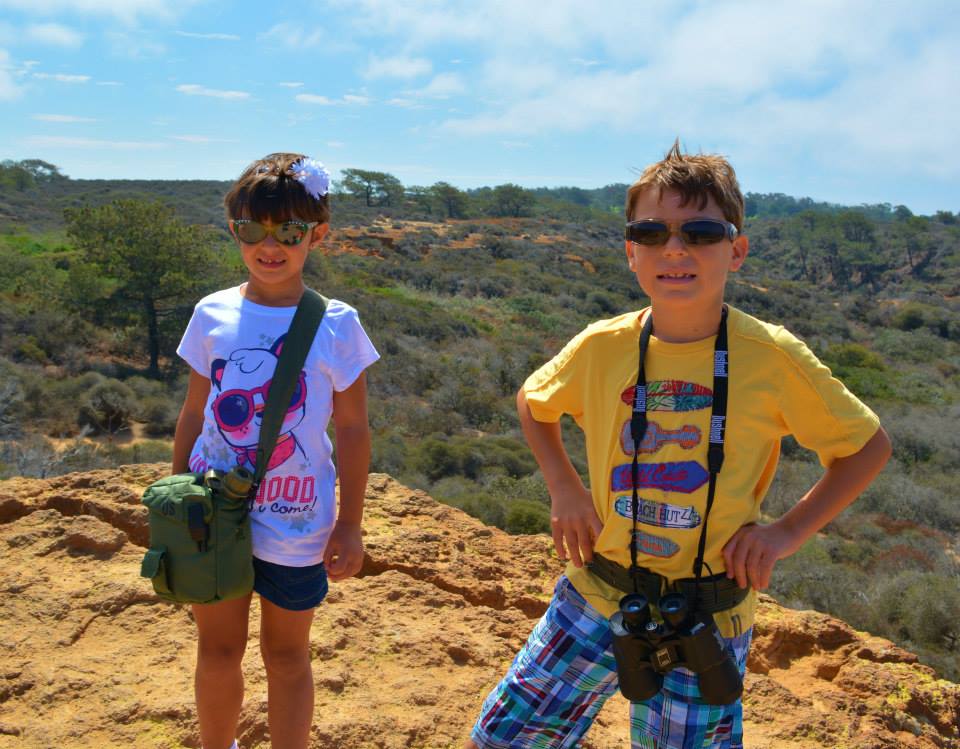 Two kids with sunglasses and binoculars hiking at Torrey Pines, San Diego