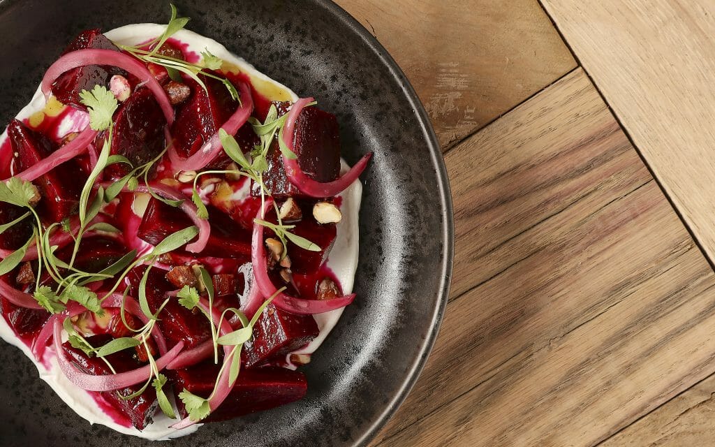 black plate on the left of image on a wood table. dark red beet salad on the plat at Small Barn Temecula