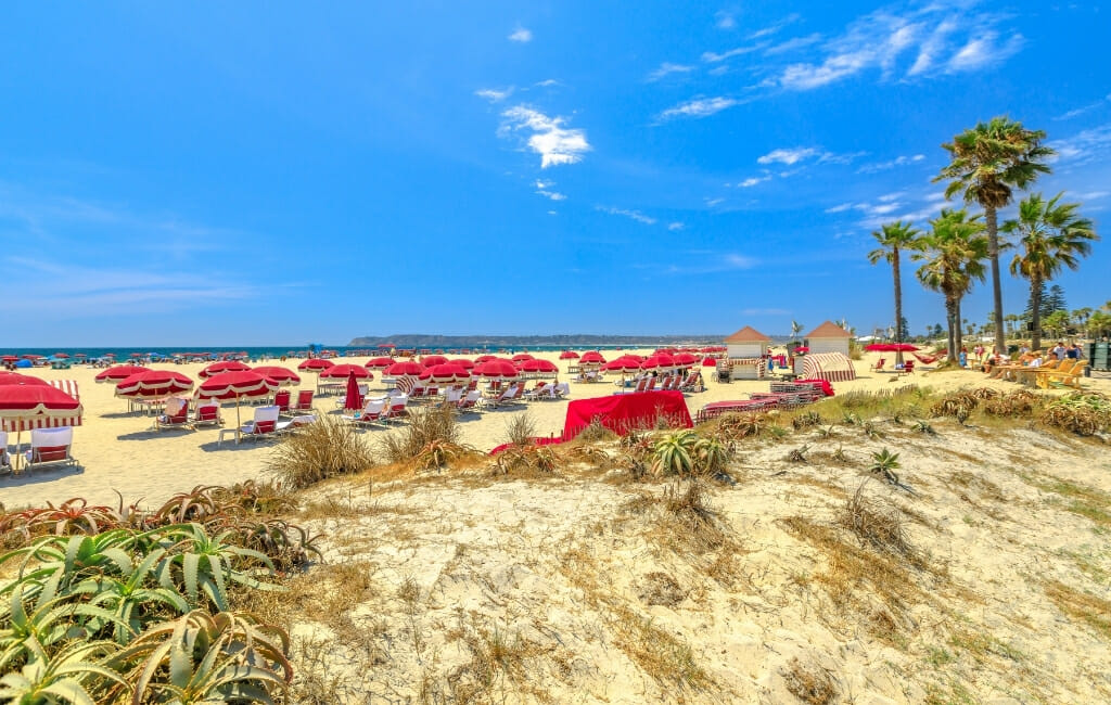 Beach in Coronado with red beach umbrellas and white chairs on a sunny day with blue sky