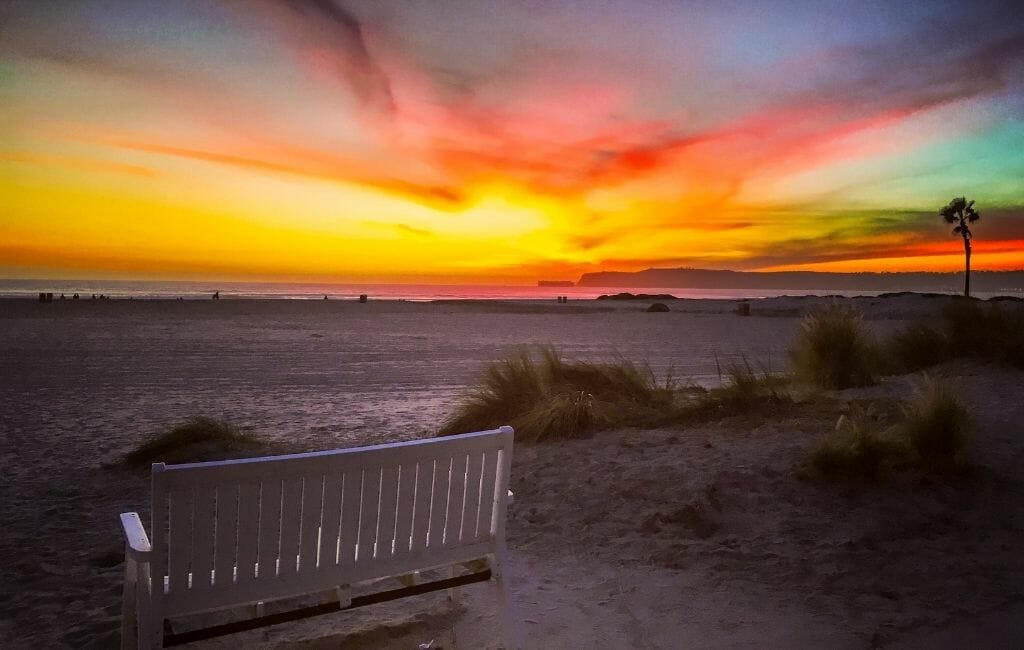 Colorful sunset on Coronado Island with white bench and sand in the foreground