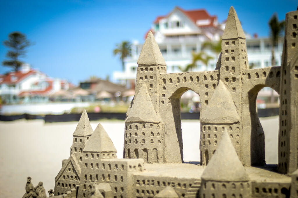 intricate sand castle in the foreground with the hotel del - white building with red roof - in the background