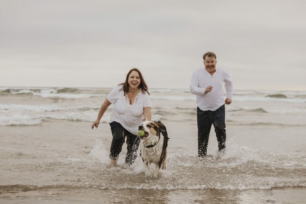 A man, a woman and a dog running through the shallow water on the dog beach in San Diego