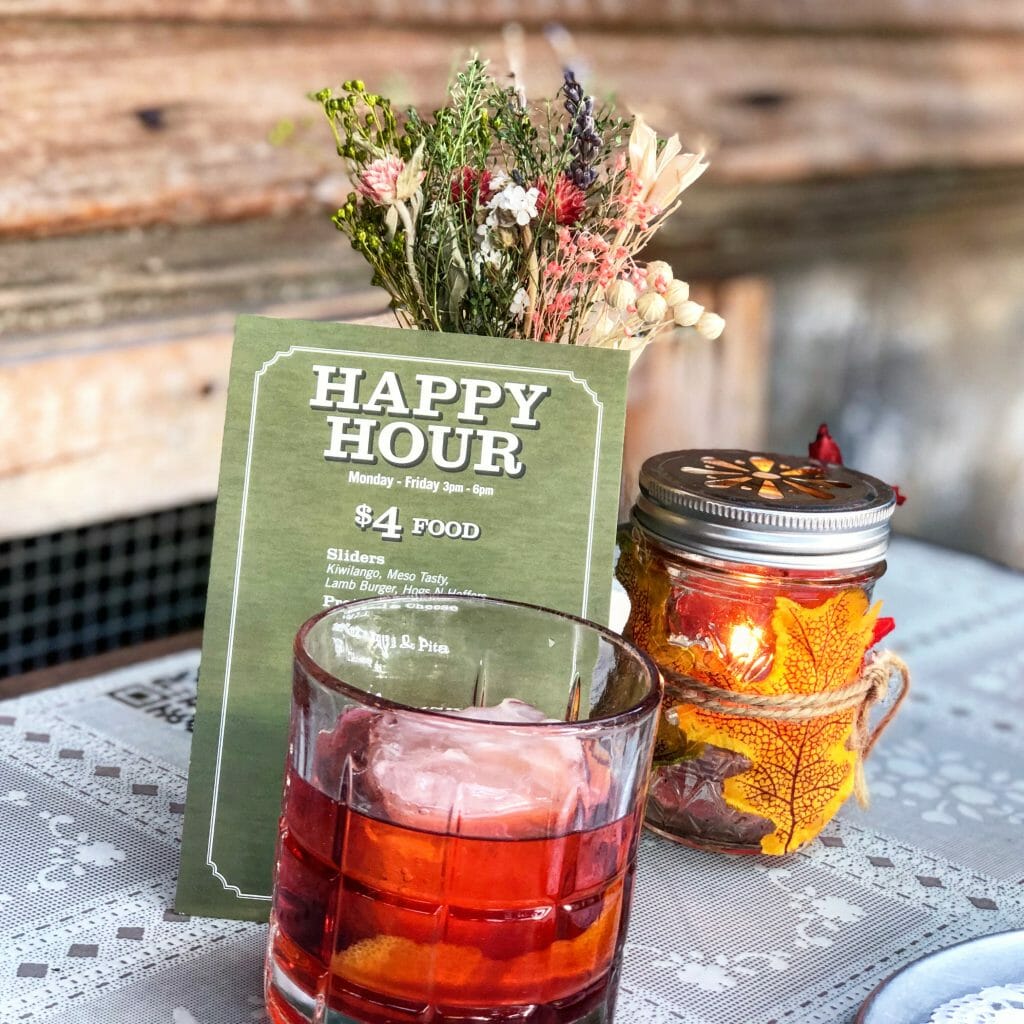 red cocktail in front of happy hour menu, yellow candle and bouquet of dried flowers