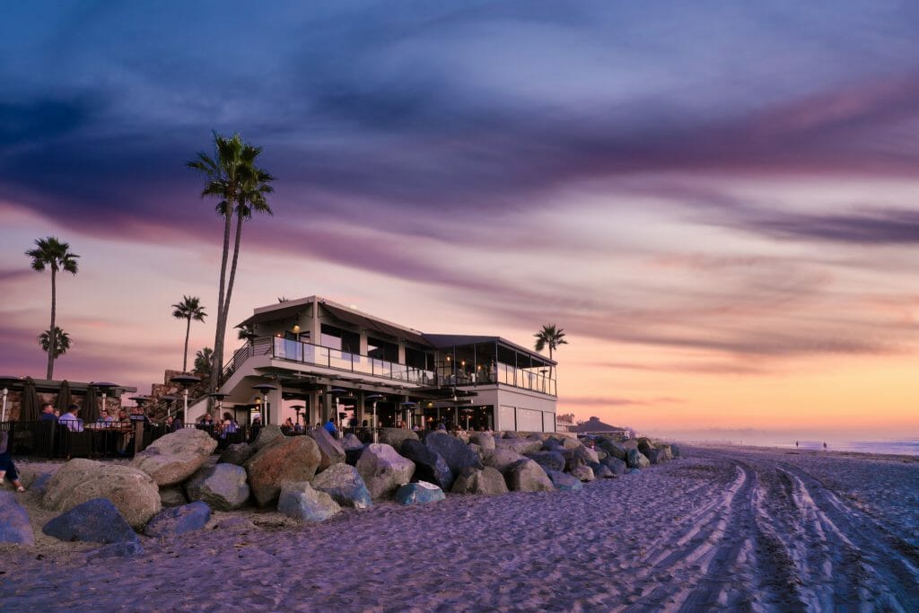 View of two story building right on the beach during sunset photographed from the beach - home to Pacific Coast Grill 