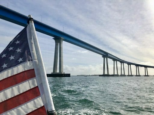 View from back of the boat with american flag on the left and looking up at the tall pilars of the curved Coronado Bay Bridge