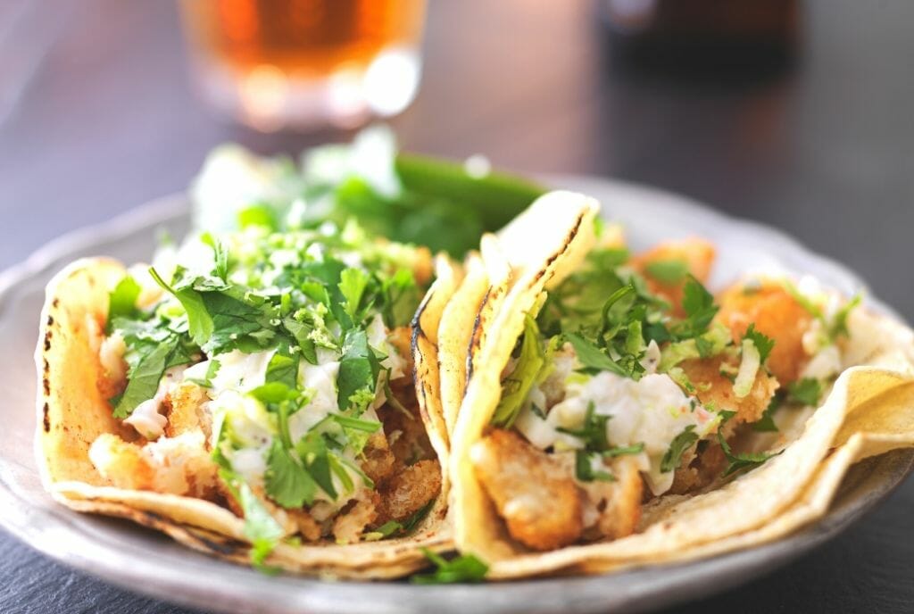 two fish tacos on a plate with a drink blurry in the background - Fish Tacos Petco Park San Diego