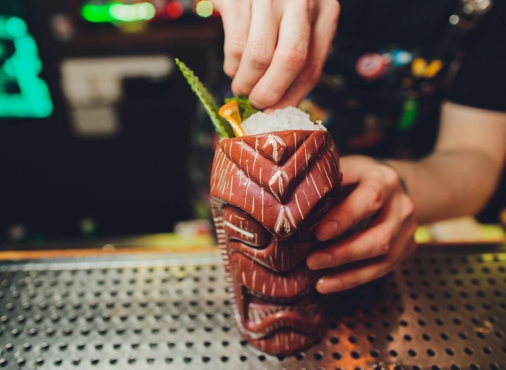 Hand reaching cocktail in tiki glass over bar counter