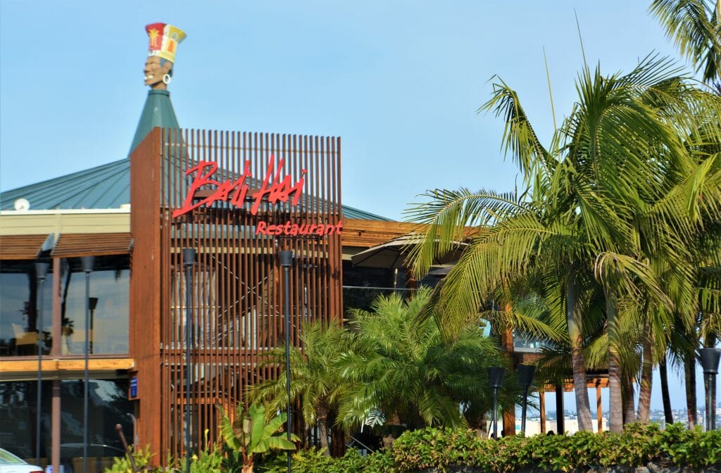 Bali Hai Restaurant San Diego - two story hut-inspired building with glass sides surrounded by palm trees - red sign on roof: Bali Hai