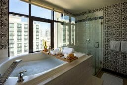 Hotel bathroom with tub filled with bubble bath and a tray with wine food and other treats