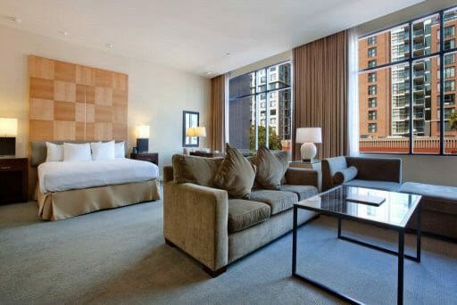 Hotel room at the Hilton Gaslamp San Diego with bed, two couches, table and large window front looking at urban scene