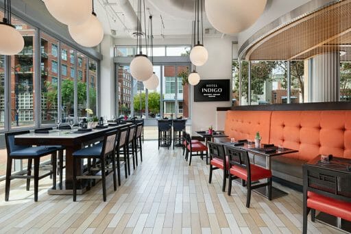 Restaurant at Hotel Indigo - Dark wood tables and chairs, orange accent wall and large white globe chandeliers 