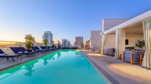 Rooftop pool at the Andaz San Diego with private cabanas on the right side and lounge chairs in the left side, pool in the middle, San Diego skyline in the background 