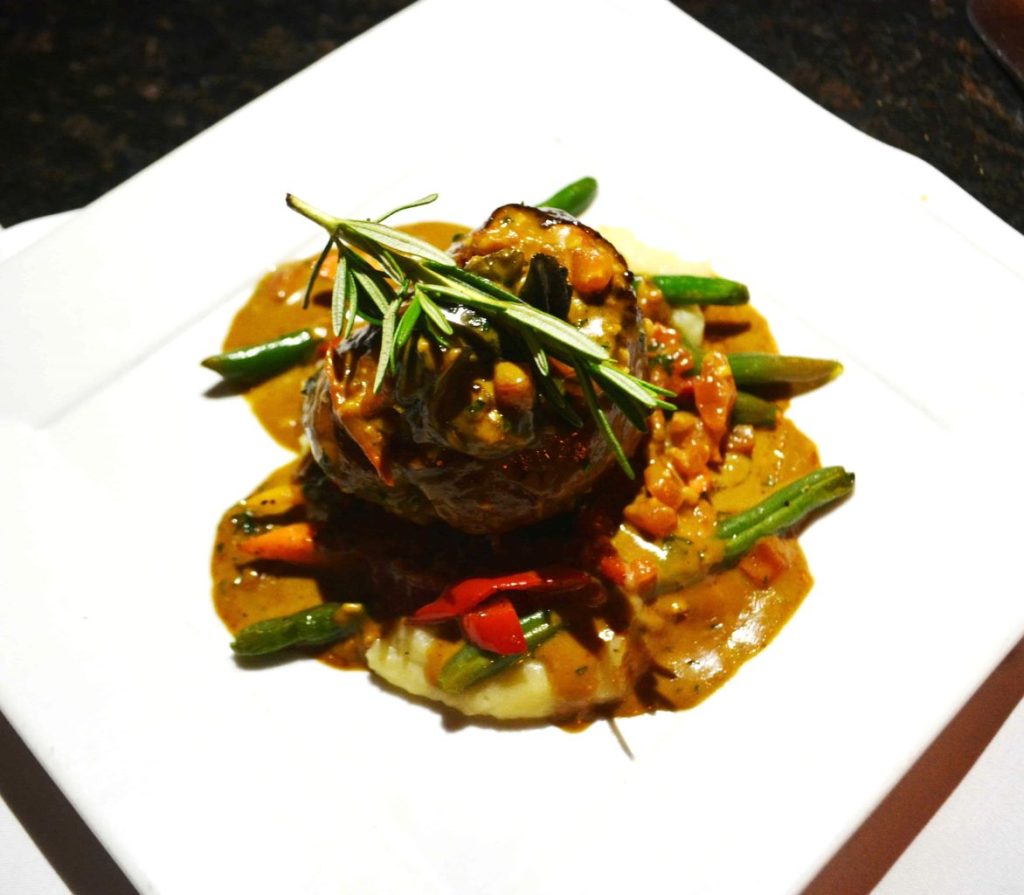 Filet Mignon with gravy, green beans, and a sprig of rosemary on a white plate at Dobsons restaurant in San Diego