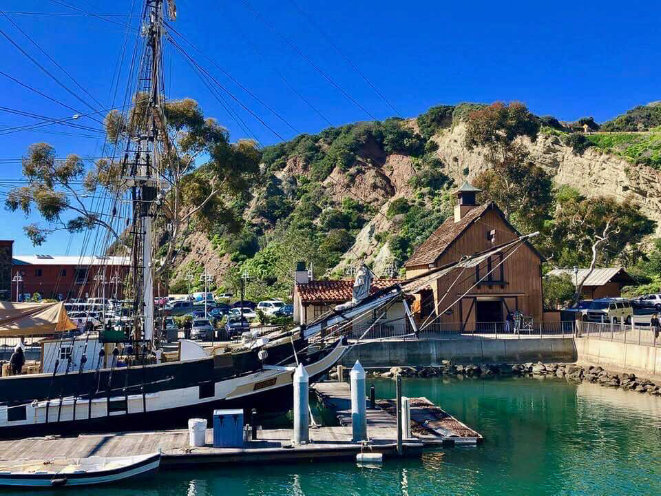 Small Marina with large wood Sailboat in front of a wood house in front of a cliff at Dana Point Harbor