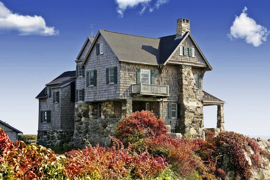 2 story house with stone exterior. Blue sky with clouds. Bushes.