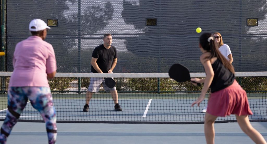 Group of four adults playing pickleball on outdoor court during summer. San Diego Pickleball Courts.