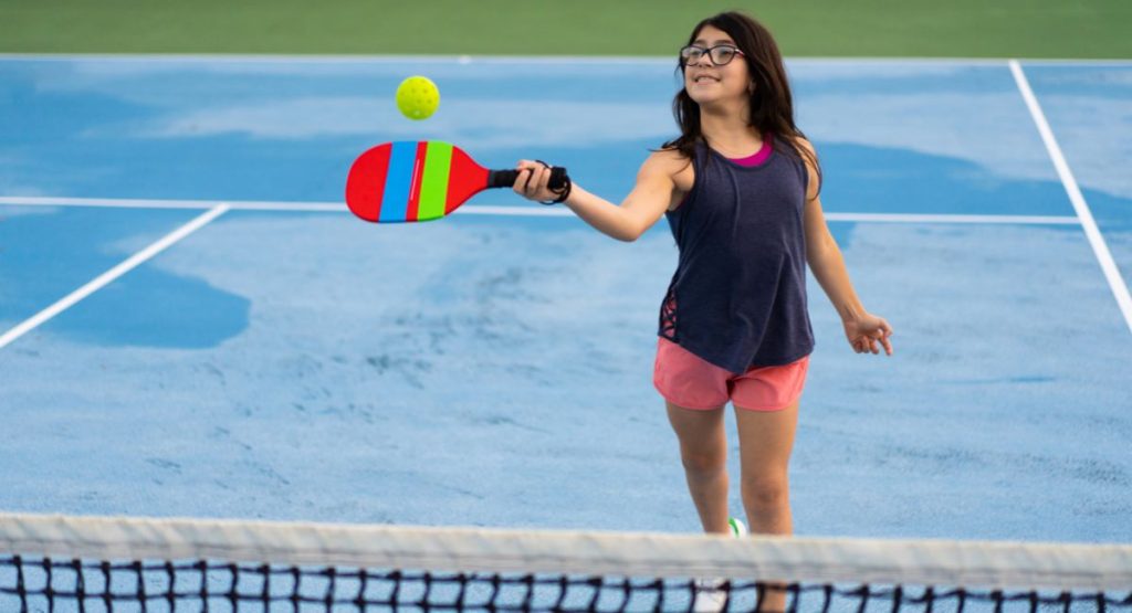 Young girl playing pickleball on blue court on sunny summer day. Pickleball Courts San Diego.