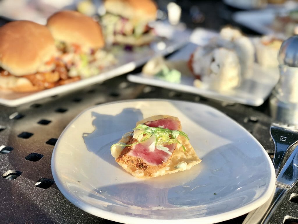 Ahi tuna on nacho tortilla chips on a white plate with other plates of food out of focus in the background