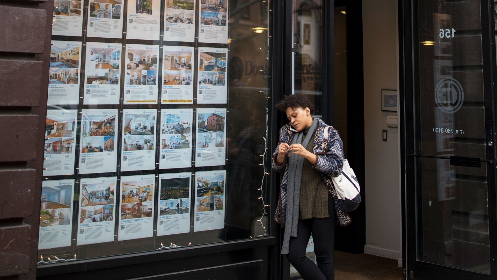 A woman having a phone call in front of a real estate agency's office
