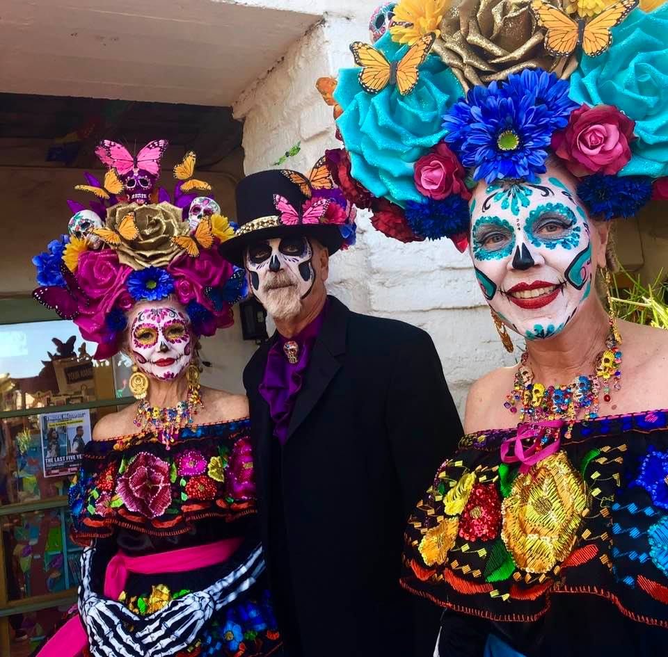 Two women and one man with traditional day of the dead costume and sugar skull makeup