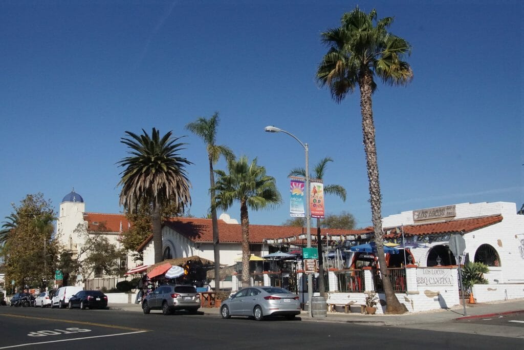 On a clear day, pedestrians walk around Old Town San Diego and its mexican style buildings