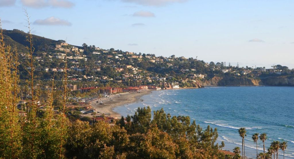 Tree and house covered mountains overlooking Pacific Ocean beach during sunset. La Jolla Shores Beach, Snorkeling in La Jolla.